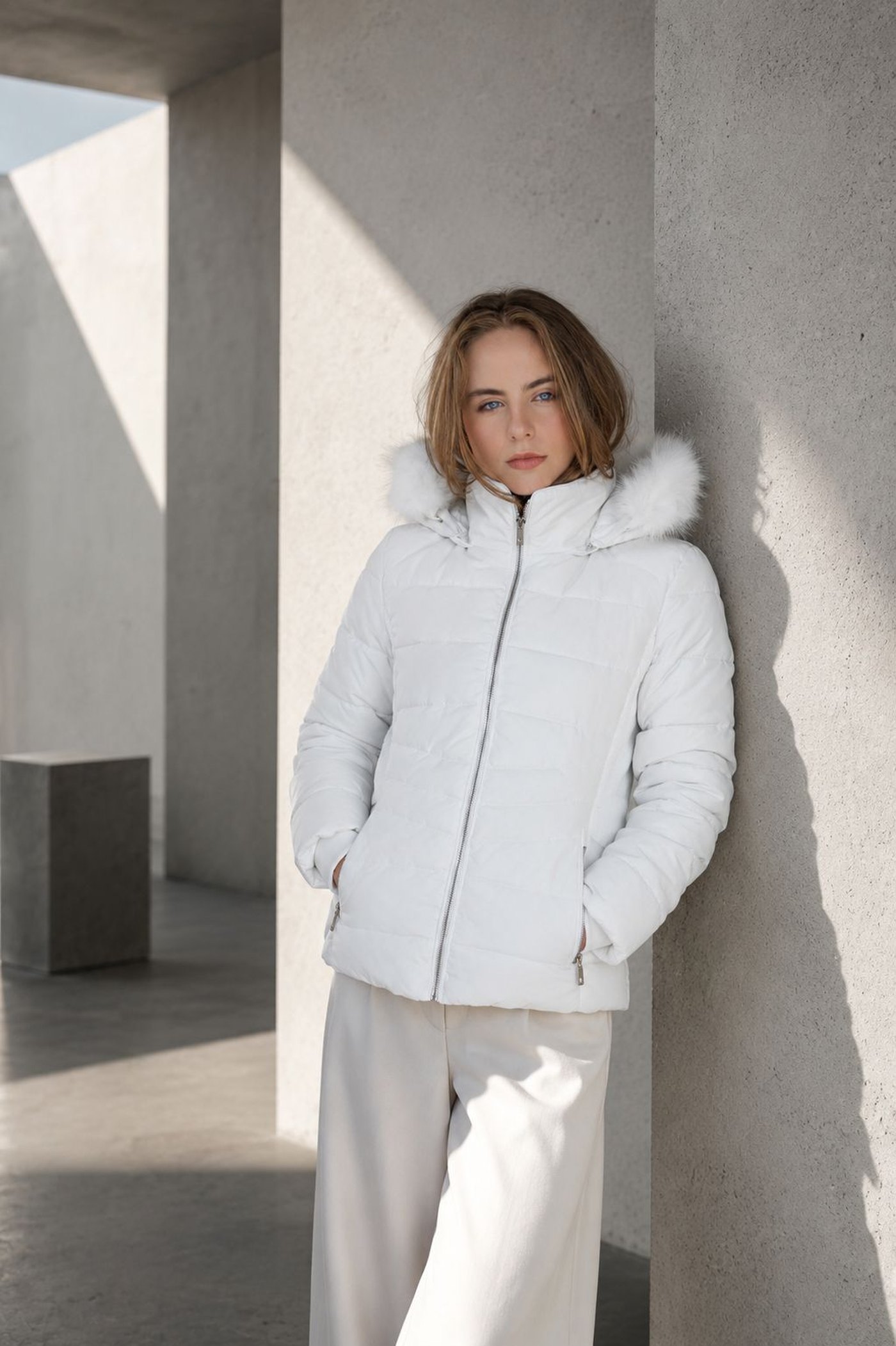 Modelo em puffer branca com capuz de pelo, apoiada em coluna de concreto